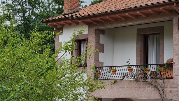 Un bâtiment traditionnel avec un toit en tuiles, une cheminée en briques et un balcon orné de plantes en pot.