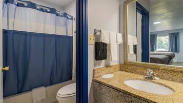 Une salle de bain avec un rideau de douche, des toilettes, un lavabo avec un miroir et un porte-serviettes.