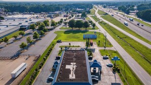 An aerial view of a parking lot with a large building, multiple lanes of traffic, and surrounding greenery.