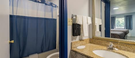 A bathroom with a shower curtain, toilet, sink, and a large mirror.
