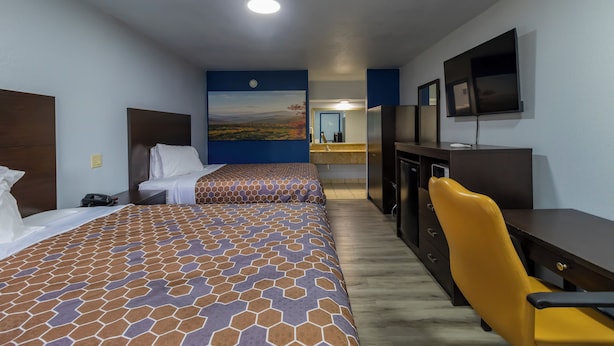 A hotel room with two beds, a desk, a chair, a TV, and a painting on the wall.