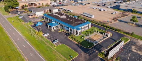 An aerial view of a commercial area with a large parking lot, a gas station, and a building with a blue roof.