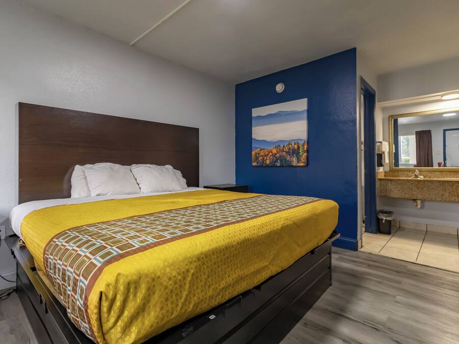 A hotel room with a bed, a painting, a bathroom with a mirror, and a sink.