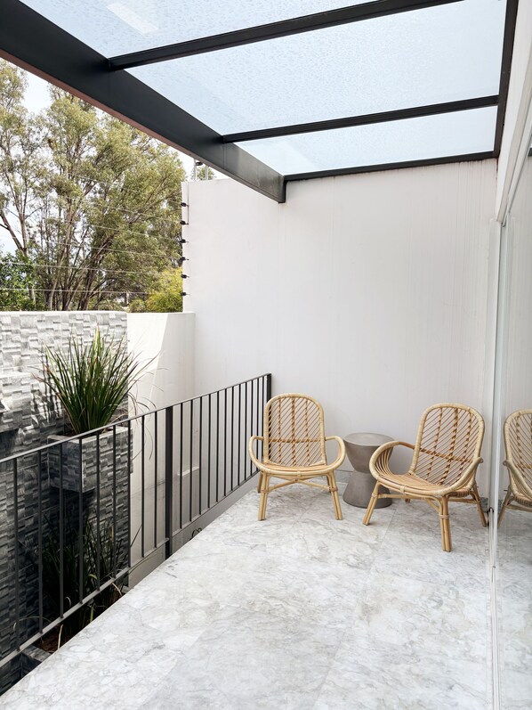 A balcony with two wicker chairs, a stone wall, and a glass railing.