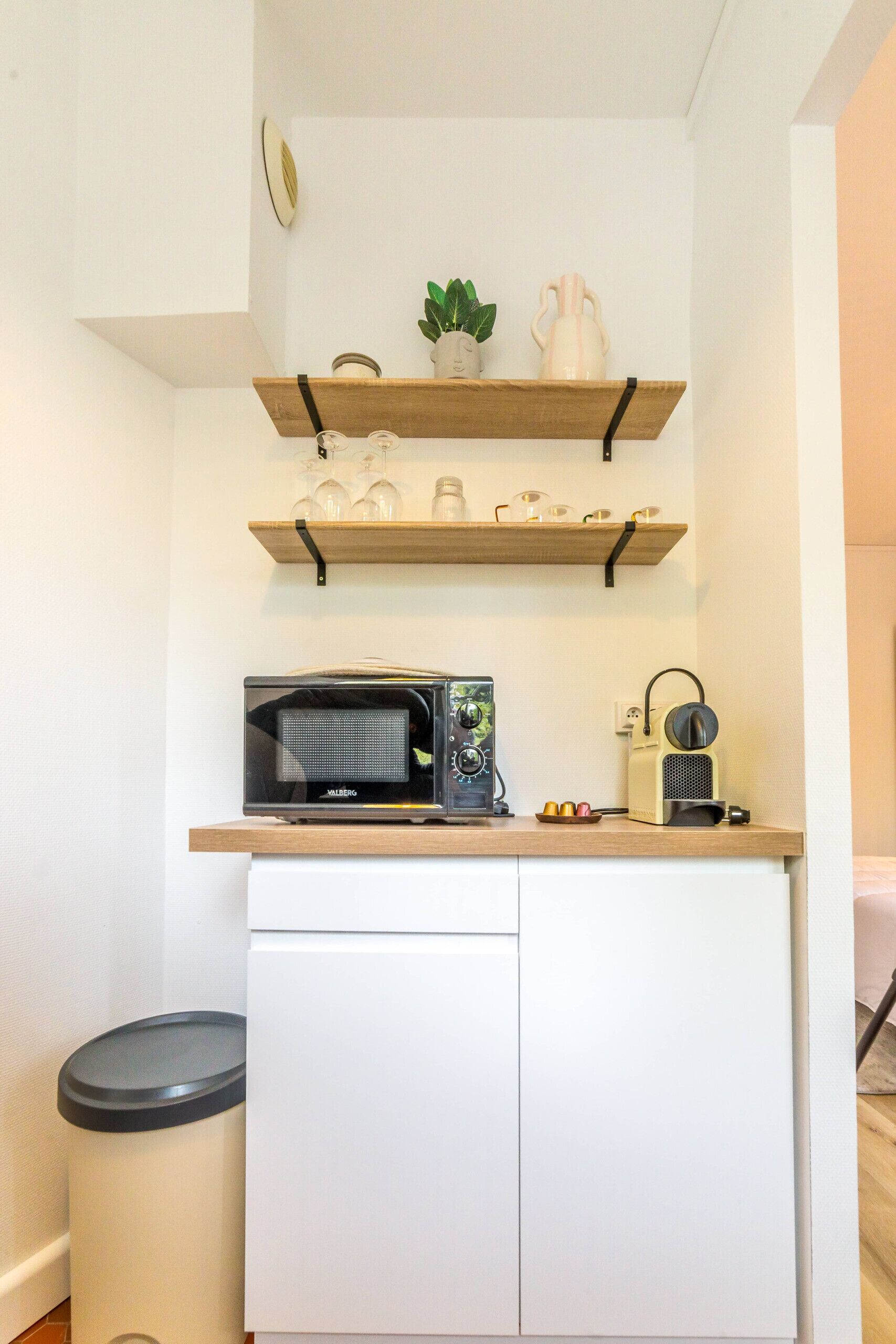 A compact kitchenette with a microwave, coffee maker, and shelves above.