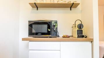A compact kitchenette with a microwave, coffee maker, and shelves above.