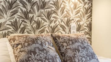 A neatly made bed with a floral-patterned pillow and a wall with a leafy pattern.