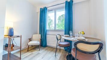 Huone, jossa on ruokapöytä, tuoleja, lamppu, patteri ja ikkuna, jossa on verhot.
