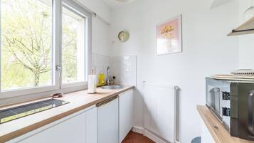 A kitchen with a window, white cabinets, a sink, a clock, and a radiator.