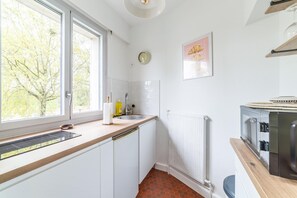 A kitchen with a window, white cabinets, a sink, a clock, and a radiator.