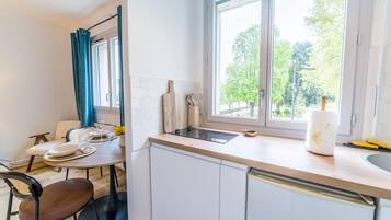 A kitchen with white cabinets, a window with a view of trees, a dining table with chairs, and a countertop with a sink and utensils.