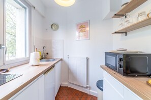 A compact kitchen with a window, a microwave, a sink, and a radiator. - L'ICONE DE LA GUIERLE (Brive-la-Gaillarde)