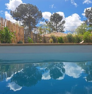 A clear pool with reflections of trees and a wooden fence. - Modern house with a pool, nestled between the lake and the forest (Lacanau)