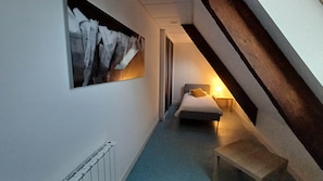 Ein schmaler Flur mit einem Bett am Ende, einem Heizkörper und einem an der Wand hängenden Kunstwerk.