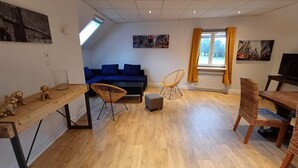 Ein modernes Wohnzimmer mit einem blauen Sofa, Korbstühlen, einem Holztisch und Kunstwerken an den Wänden.