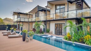 A modern two-story house with a swimming pool, outdoor seating, and lush landscaping.