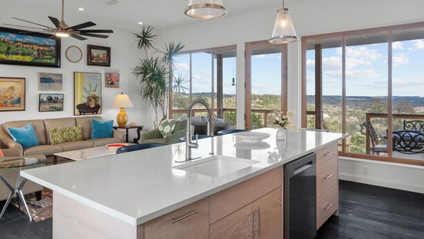 A modern kitchen with a large island, a ceiling fan, and large windows offering a view of the landscape.