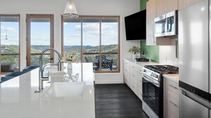 A modern kitchen with a large island, stainless steel appliances, and a view of the landscape through large windows.
