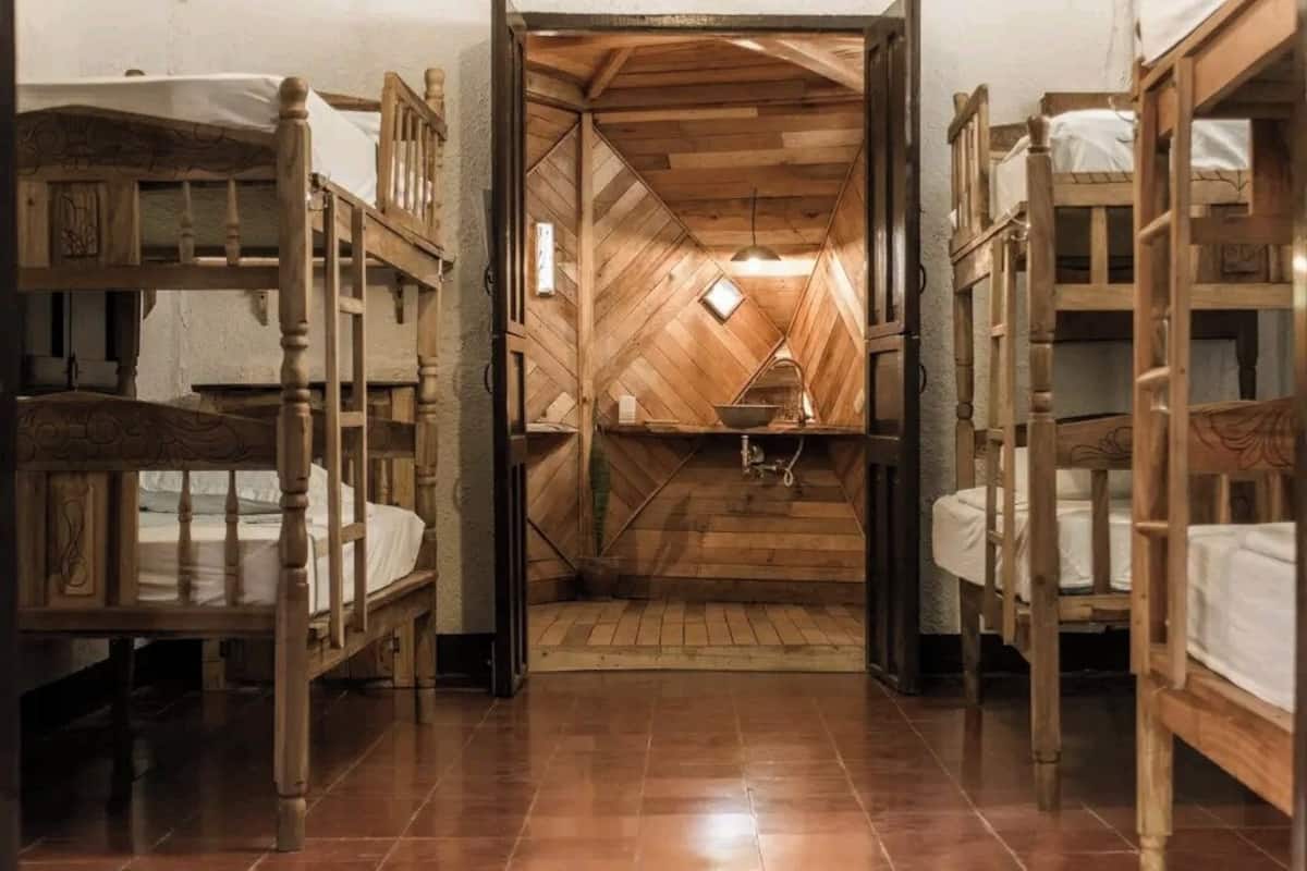 A dormitory room with bunk beds, a wooden ceiling, and a small kitchen area.