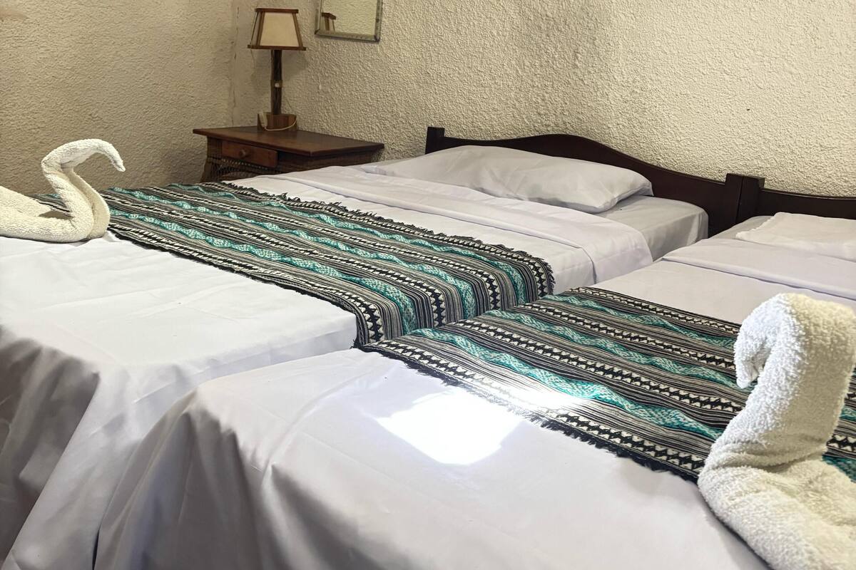 A hotel room with two beds, a nightstand, a lamp, and a mirror on the wall.