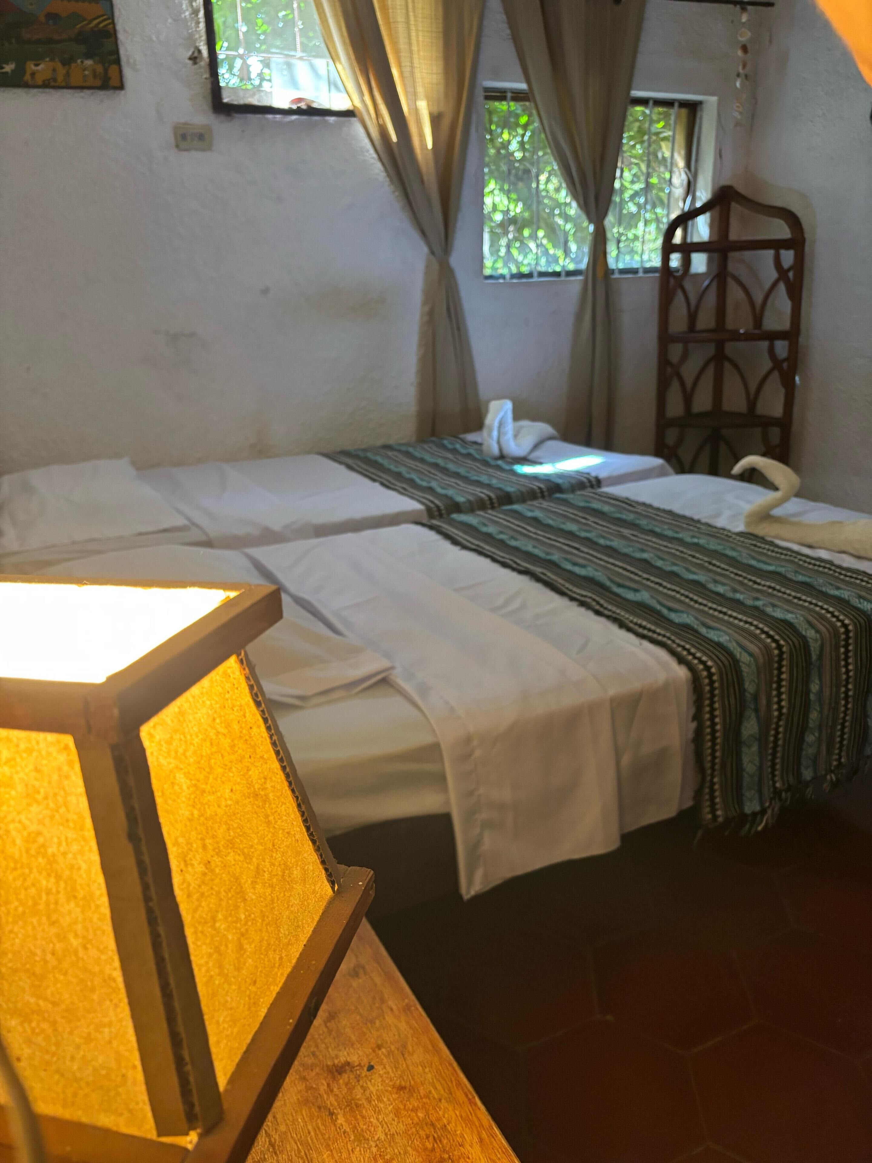 A single bed with a striped blanket, a bedside lamp, and a window with curtains.