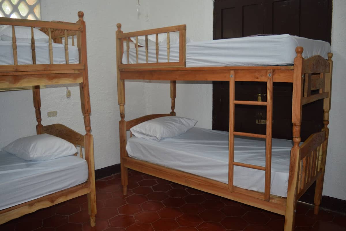 Two wooden bunk beds with white bedding in a room with tiled flooring and a dark door in the background.