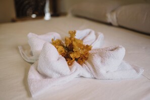 A neatly folded white towel with a bouquet of yellow flowers on a wooden surface. - caracolito hostal (Leon)