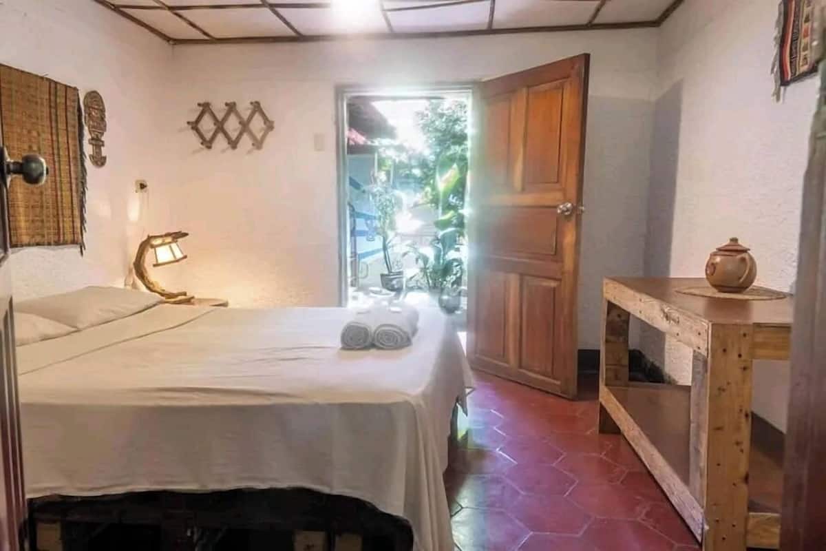 A room with a bed, a table with a pot, and a door leading outside.