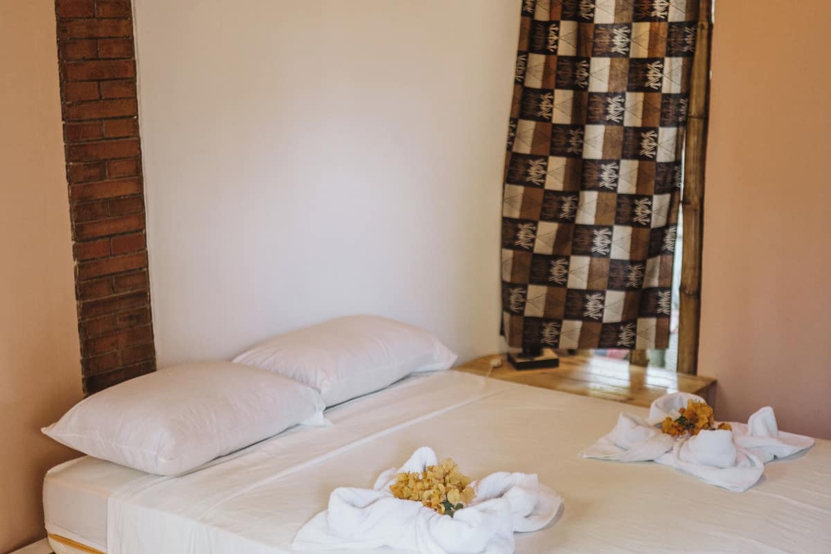 A bed with white linens, two pillows, and a floral arrangement on the bed.