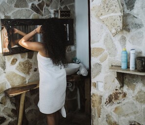 A person in a white towel standing in front of a mirror in a bathroom with a stone wall. - caracolito hostal (Leon)