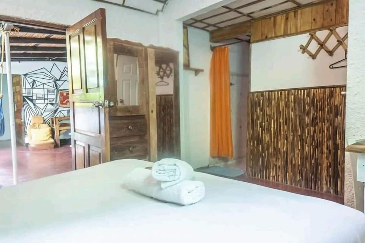 A hotel room with a bed, a wooden door, a towel, and a wall with a textured pattern.