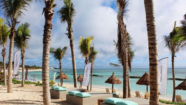 Ein Strand mit Palmen, Liegestühlen und einer Laube aus Palmzweigen.