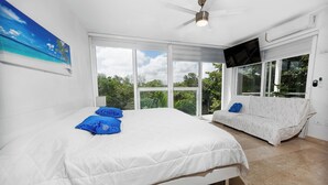 Ein Schlafzimmer mit einem großen Bett, einer Couch, einem Deckenventilator und einem an der Wand befestigten Fernseher.