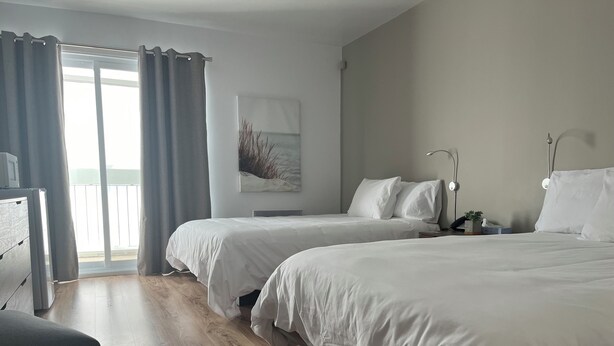 A hotel room with two beds, a desk, and a view of the outside. - HĂ´tel Normandie (Rimouski)