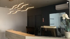 A reception area with a modern design, featuring a wooden reception desk, a black counter, and a geometric patterned wall. - HĂ´tel Normandie (Rimouski)