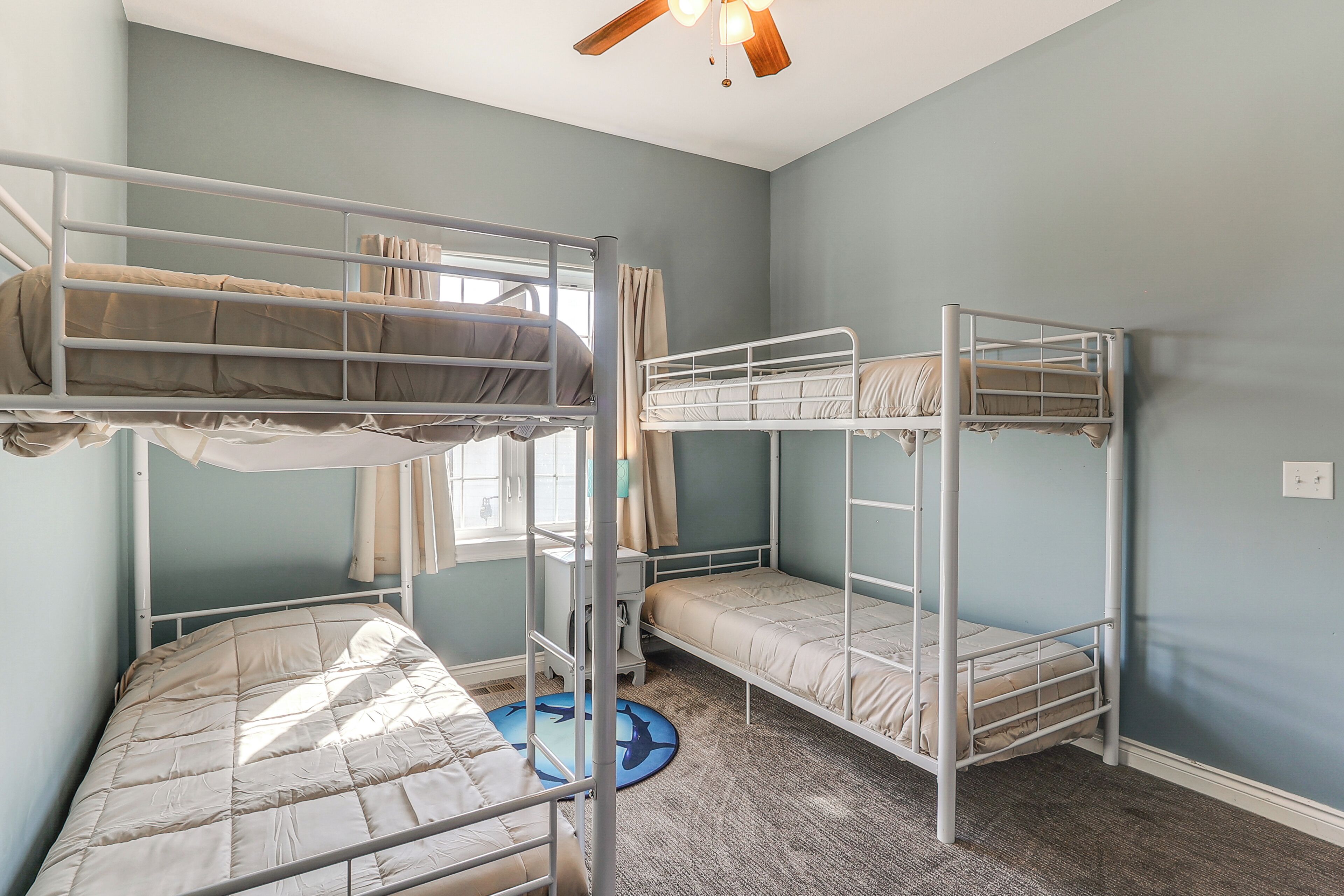 Une chambre avec des lits superposés, un ventilateur de plafond et une fenêtre avec des rideaux.