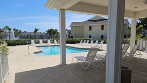 A covered pool area with lounge chairs, a clear pool, and a view of residential buildings in the background.