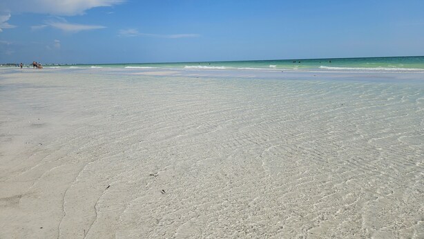 A wide, sandy beach with gentle waves and a clear blue sky.