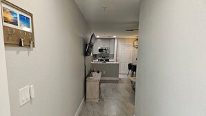 A hallway leading to a kitchen with a marble floor, a dining area, and a chandelier.