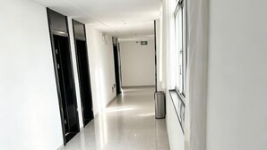 Un long couloir étroit, doté d’un sol brillant, avec des portes noires d’un côté et une poubelle sur la droite.