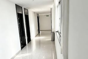 A long, narrow hallway with a shiny floor, black doors on one side, and a trash can on the right. - Aihang Alliance Hotel (Lianyungang)