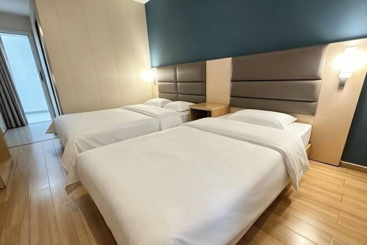 Une chambre d’hôtel avec deux lits, un plancher en bois, une tête de lit moderne et des lampes de chevet.