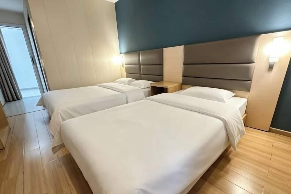Hotellihuone, jossa on kaksi sänkyä, puulattia, moderni sängynpääty ja yöpöytävalaisimet.