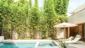 A modern outdoor pool area with a wooden fence, lounge chairs, and a large umbrella.
