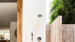A modern outdoor shower area with a wooden deck, surrounded by a wooden fence and a small garden.