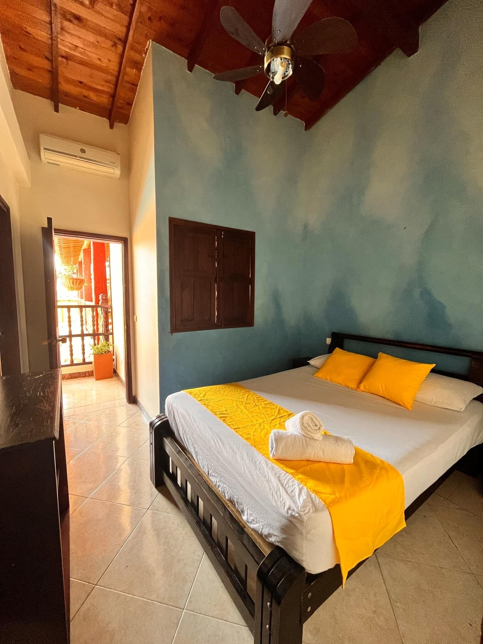 A bedroom with a bed, a ceiling fan, a wooden door, and a window.