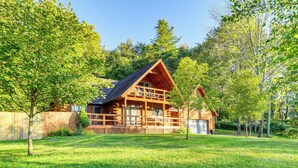 A log cabin with a porch, surrounded by a well-maintained lawn and trees. - Modern Comforts Classic Cabin: Family/Fish Escape! (Deposit)