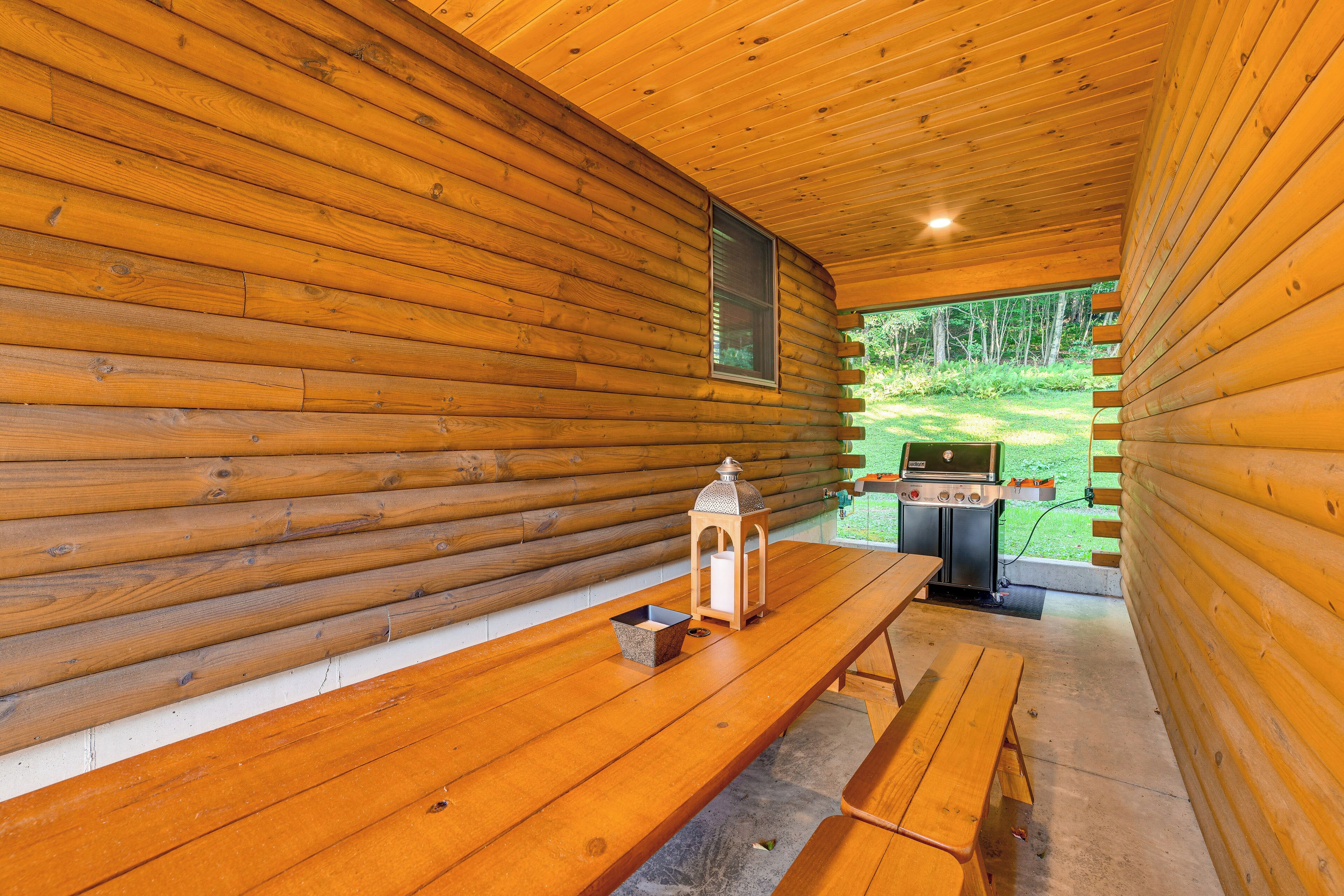 A wooden cabin interior with a dining table, a lantern, and a grill outside.