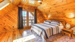 A cozy attic bedroom with wooden walls and a sloped ceiling, featuring a large bed, a nightstand, and a ceiling fan. - Modern Comforts Classic Cabin: Family/Fish Escape! (Deposit)
