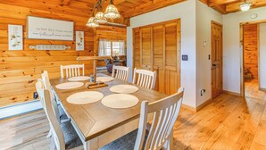 A wooden dining room with a large table, chairs, and a chandelier. - Modern Comforts Classic Cabin: Family/Fish Escape! (Deposit)